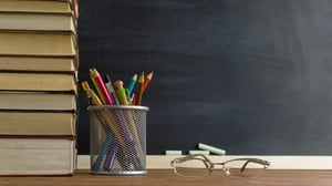 Teacher's desk with books,writing utensils, and glasses on top